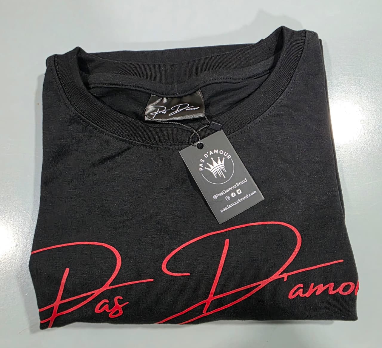Folded black t-shirt with red text and a tag on a light gray background